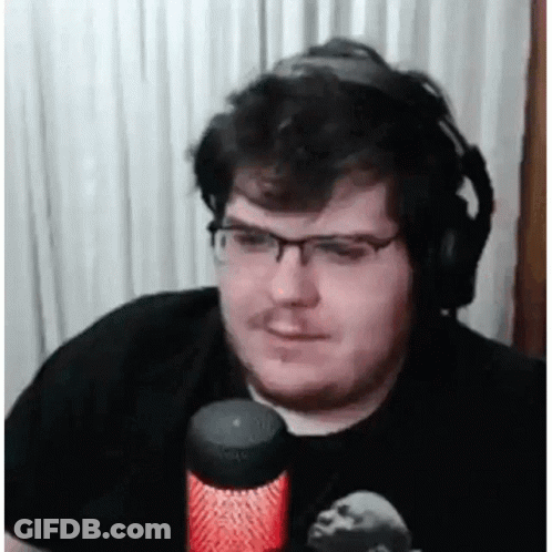 A Man Wearing Headphones And Glasses Is Sitting In Front Of A Microphone And Smiling . GIF