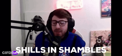 A Man Wearing Headphones And Glasses Is Sitting In Front Of A Microphone With The Words " Shills In Shambles " Above Him GIF