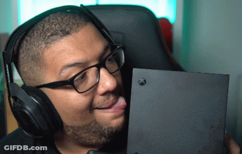 A Man Wearing Headphones And Glasses Is Sticking His Tongue Out At An Xbox Box GIF