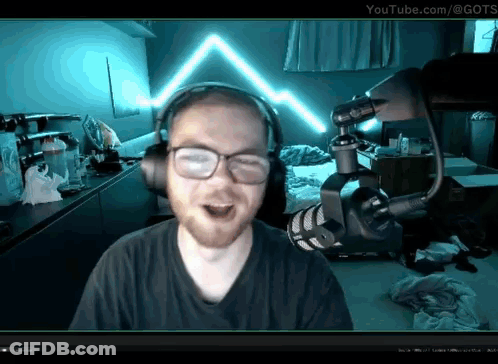 A Man Wearing Headphones And Glasses Stands In Front Of A Microphone With Youtube.com In The Corner GIF