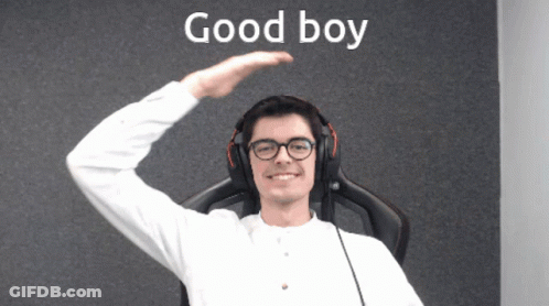 A Man Wearing Headphones And Glasses Stands In Front Of A Wall That Says Good Boy GIF