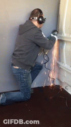 A Man Wearing Headphones And Goggles Is Using A Grinder To Cut A Piece Of Metal GIF