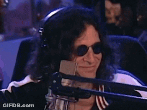 A Man Wearing Headphones And Sunglasses Is Smiling In Front Of A Microphone . GIF