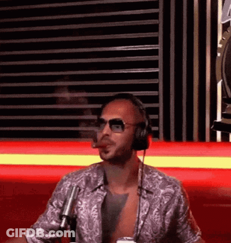 A Man Wearing Headphones And Sunglasses Is Smoking A Cigar While Sitting In Front Of A Microphone . GIF