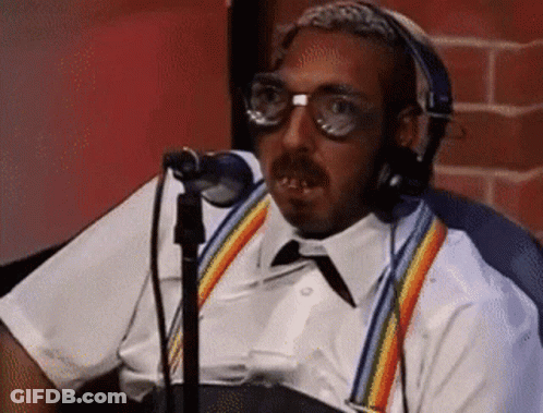 A Man Wearing Headphones And Suspenders Is Sitting In Front Of A Microphone . GIF