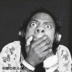A Man Wearing Headphones Is Covering His Mouth With His Hand And Making A Funny Face . GIF