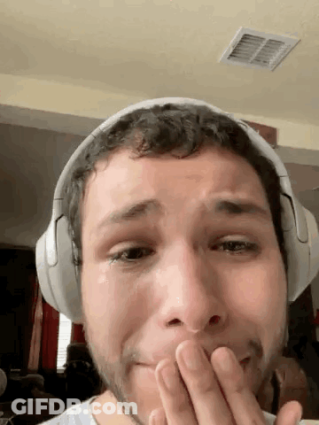 A Man Wearing Headphones Is Covering His Mouth With His Hand While Crying . GIF
