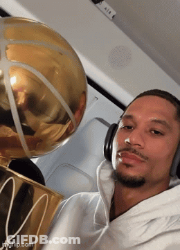 A Man Wearing Headphones Is Holding A Basketball Trophy With The Letter M On It GIF
