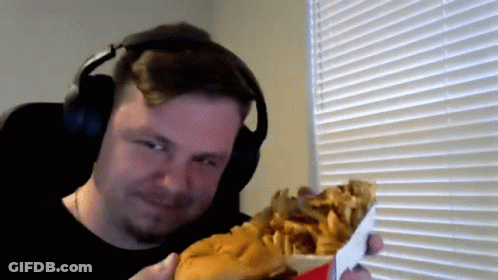 A Man Wearing Headphones Is Holding A Large Hamburger And French Fries GIF