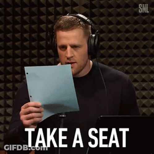 A Man Wearing Headphones Is Holding A Piece Of Paper With The Words Take A Seat Written On It . GIF