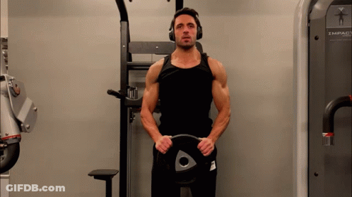 A Man Wearing Headphones Is Holding A Weight Plate With An Arrow On It GIF
