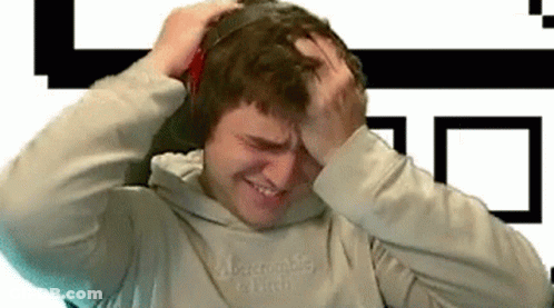 A Man Wearing Headphones Is Holding His Head And Making A Funny Face . GIF