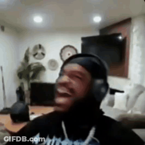 A Man Wearing Headphones Is Laughing In A Living Room While Sitting On A Couch . GIF