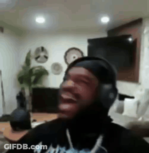 A Man Wearing Headphones Is Laughing In A Living Room While Sitting On A Couch . GIF