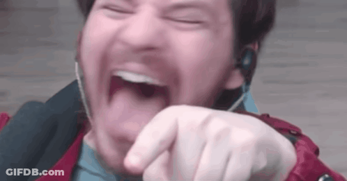 A Man Wearing Headphones Is Laughing With His Mouth Open And Pointing At The Camera . GIF