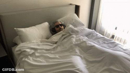 A Man Wearing Headphones Is Laying On A Bed GIF
