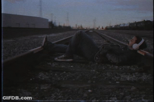 A Man Wearing Headphones Is Laying On The Train Tracks GIF