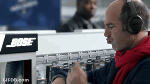 A Man Wearing Headphones Is Looking At His Watch In Front Of A Bose Sign GIF