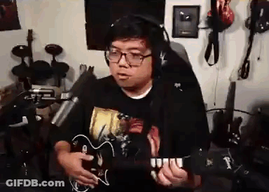 A Man Wearing Headphones Is Playing A Guitar In Front Of A Microphone In A Room . GIF