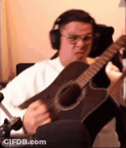 A Man Wearing Headphones Is Playing An Acoustic Guitar In A Room . GIF