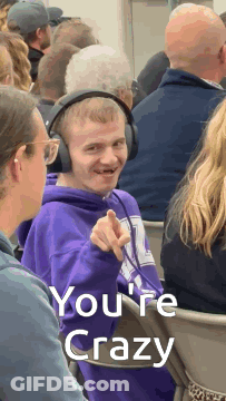 A Man Wearing Headphones Is Pointing At The Camera With The Words You 'Re Crazy Behind Him GIF
