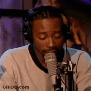 A Man Wearing Headphones Is Singing Into A Microphone In A Studio . GIF