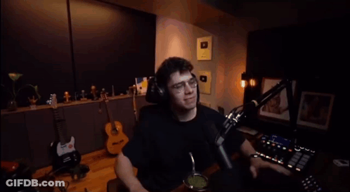 A Man Wearing Headphones Is Sitting In Front Of A Microphone And Waving His Hand GIF