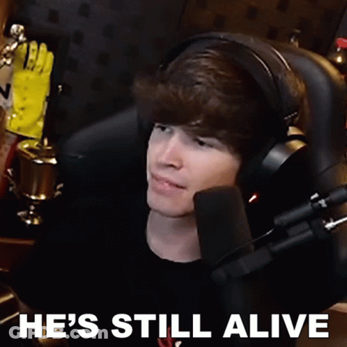 A Man Wearing Headphones Is Sitting In Front Of A Microphone With The Words He 'S Still Alive Written Below Him GIF