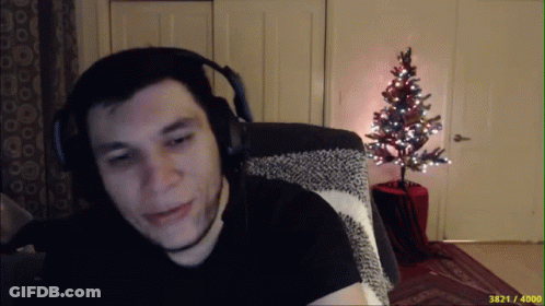 A Man Wearing Headphones Is Sitting In Front Of A Small Christmas Tree GIF