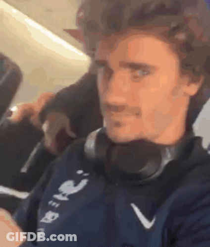 A Man Wearing Headphones Is Sitting On A Plane And Looking At His Phone . GIF