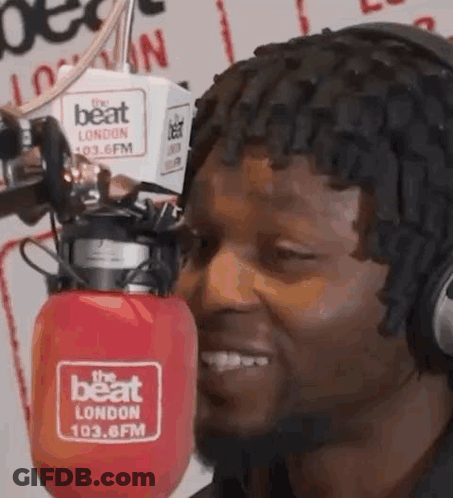 A Man Wearing Headphones Is Smiling In Front Of A Microphone In A Radio Station . GIF