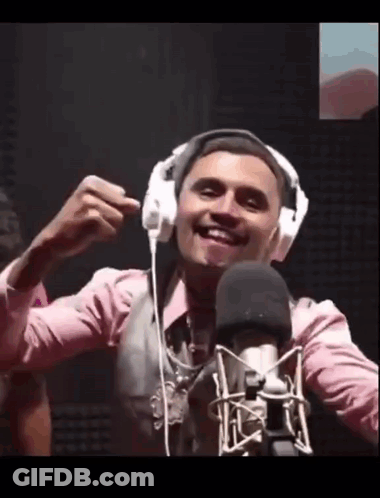A Man Wearing Headphones Is Smiling In Front Of A Microphone . GIF
