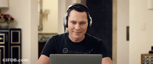 A Man Wearing Headphones Is Smiling While Looking At His Laptop GIF