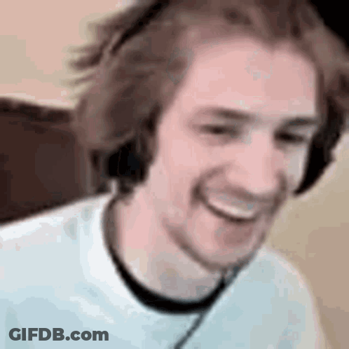 A Man Wearing Headphones Is Smiling While Sitting In Front Of A Computer . GIF