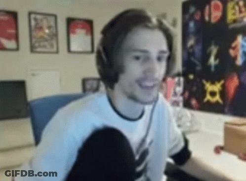 A Man Wearing Headphones Is Smiling While Sitting In Front Of A Computer In A Room . GIF