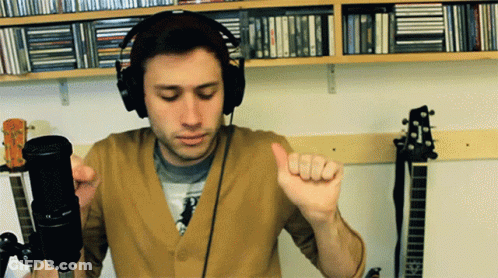 A Man Wearing Headphones Is Standing In Front Of A Microphone And Giving A Thumbs Up GIF
