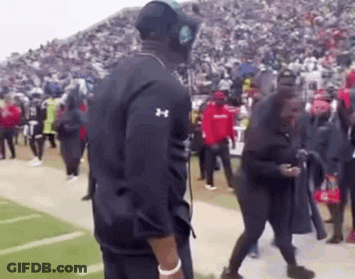 A Man Wearing Headphones Is Standing On A Football Field With A Crowd Of People . GIF