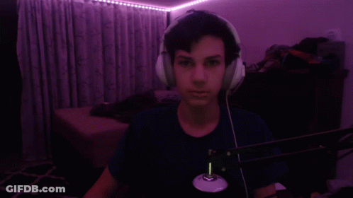 A Man Wearing Headphones Is Taking A Selfie In A Dark Room With Purple Lights Behind Him . GIF