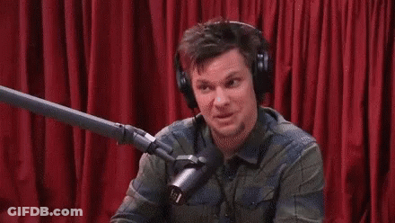 A Man Wearing Headphones Is Talking Into A Microphone In Front Of A Red Curtain GIF