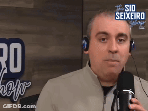 A Man Wearing Headphones Is Talking Into A Microphone In Front Of A Sign That Says The Sid Seixeiro Show GIF