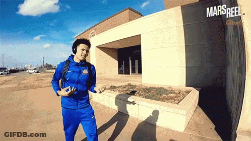 A Man Wearing Headphones Is Walking In Front Of A Building That Says Mars Reel On It GIF
