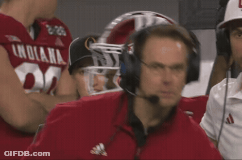 A Man Wearing Headphones Is Watching A Football Game With A Player Wearing A Jersey That Says Nebraska GIF