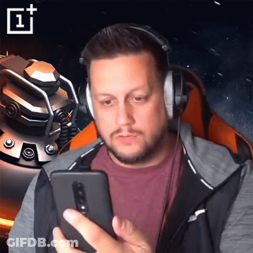 A Man Wearing Headphones Looks At His Phone With A Oneplus Logo Behind Him GIF