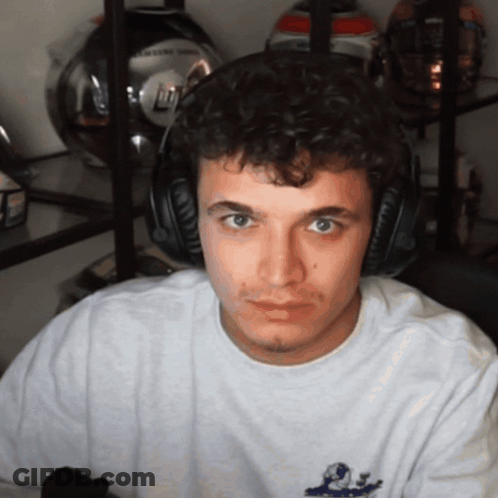 A Man Wearing Headphones Looks At The Camera In Front Of A Shelf Of Helmets GIF