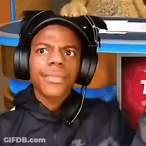 A Man Wearing Headphones Looks At The Camera With A T On The Wall Behind Him GIF
