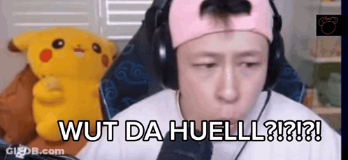 A Man Wearing Headphones Says Wut Da Huell In Front Of A Stuffed Pikachu GIF