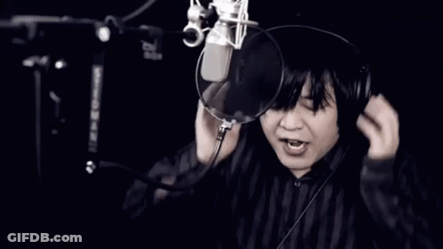 A Man Wearing Headphones Singing Into A Microphone With His Mouth Open GIF