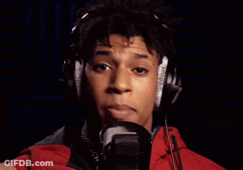 A Man Wearing Headphones Sings Into A Microphone In Front Of A Neon Open Sign GIF