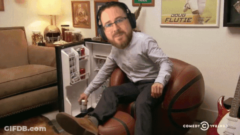 A Man Wearing Headphones Sits In A Chair In Front Of A Doug Flutie Poster GIF