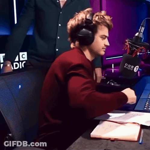 A Man Wearing Headphones Sits In Front Of A Microphone That Says BBC Radio 0 GIF